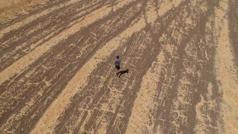 Person-running-through-arid-brown-field-from-aerial-view-with-drone