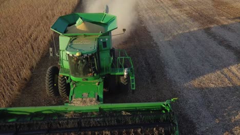 a midwest farmer harvesting a soybean field with a combine, tractor, and auger wagon