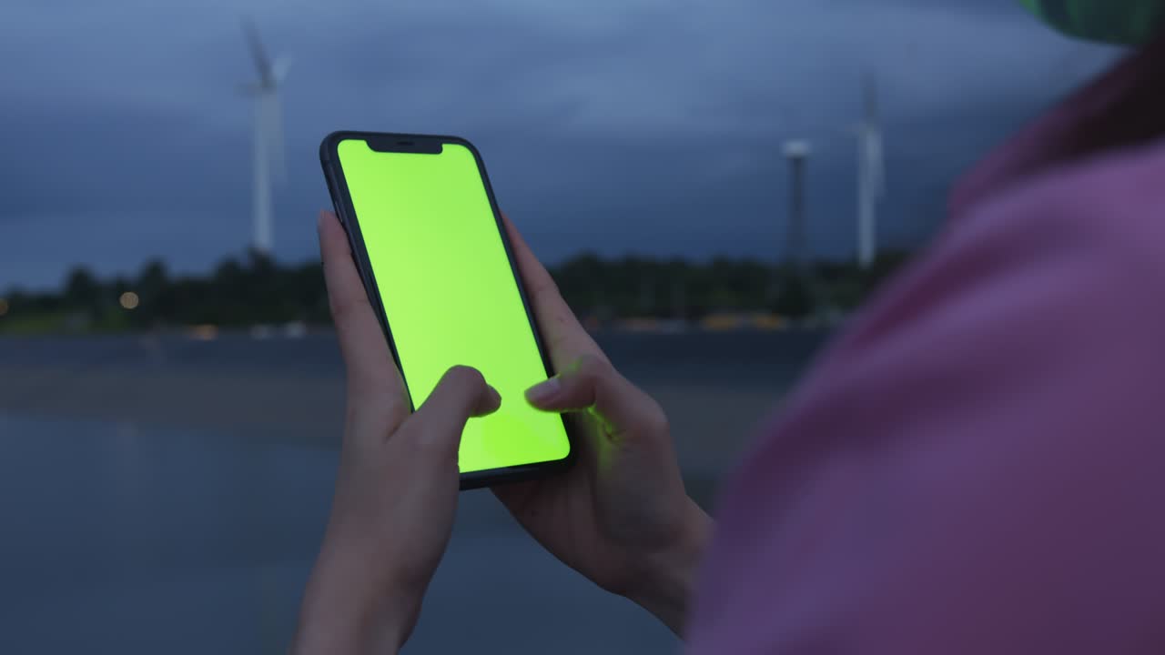 tiro de mano: mujer turista sosteniendo un teléfono de pantalla verde por la noche y una mujer usando una máscara para prevenir enfermedades.