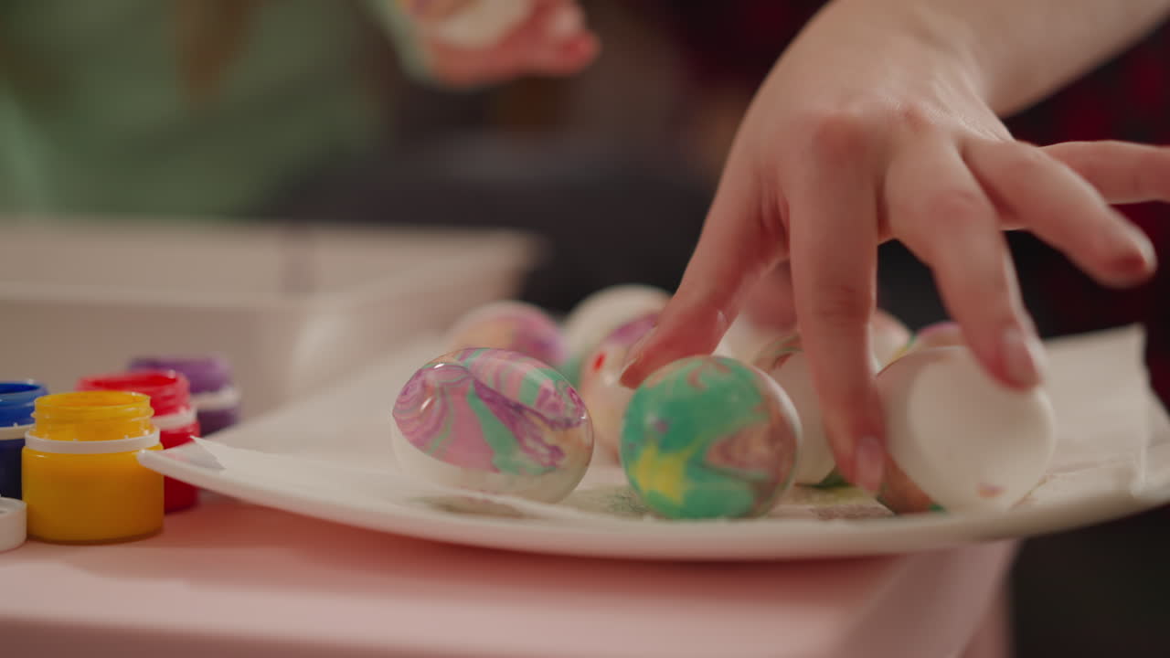Mother and daughter put decorated eggs to dry on square dish