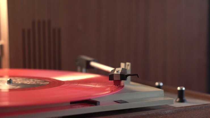 Ascoltando un disco in vinile rosso su un grammofono vintage e bevendo vino bianco nell'ambiente domestico, primo piano.
