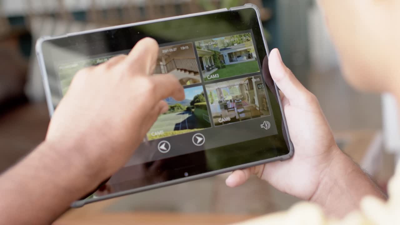 manos de un hombre biracial usando una tableta con vistas de cámaras de seguridad en la pantalla, cámara lenta