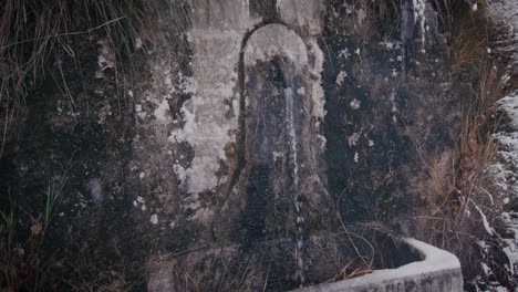 El-Agua-Fluye-Del-Grifo-De-Agua-Vintage-En-La-Pared-De-Piedra-En-El-Día-De-Invierno