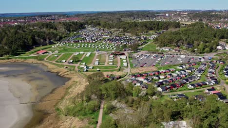 askimsbadet camping area near gothenburg, sweden. shows rows of cabins, caravans, and parking beside the sandy beach and shoreline, with forested hills and town