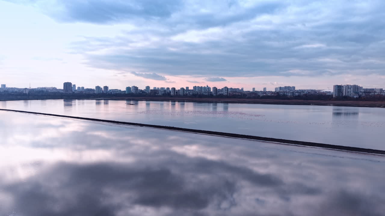 Água calma de reservatórios de evaporação de sal refletindo o céu nublado. Vista aérea minimalista de grandes tanques industriais com superfície de água lisa refletindo o céu rosa do pôr do sol.