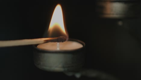 close up of a tealight in a silver candleholder being lit by a flaring match stick with a dark background a night