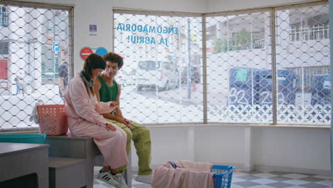 two friends washing clothes in self service. young couple talking wait laundry