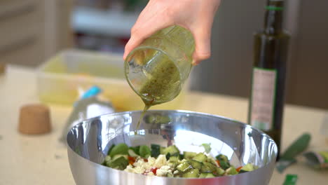 hands of a chef pouring a dressing sauce into the bowl of vegetable salad. - close up shot