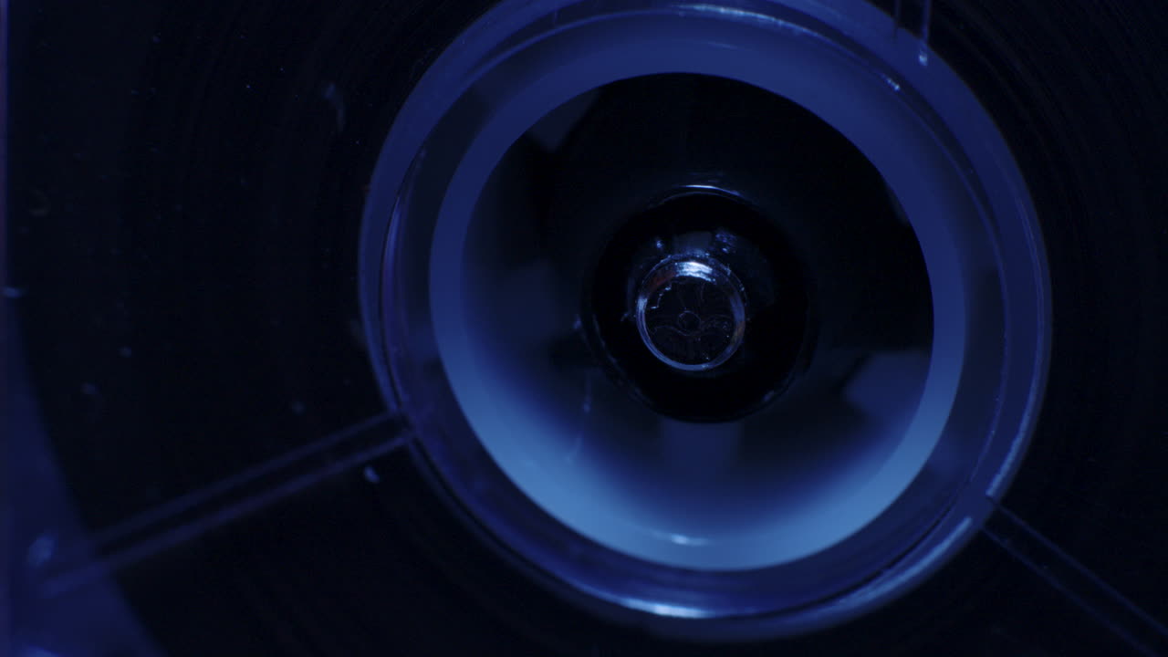 primerísimo primer plano del husillo de la grabadora de microcassette girando en la luz de colores mixtos cambiantes