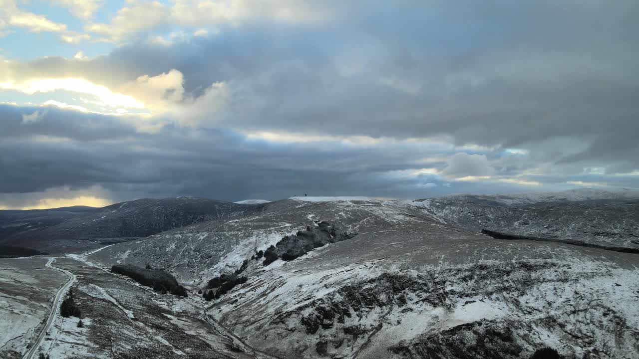 Snöigt bergslandskap med moln och solljus som tittar fram, flygvy