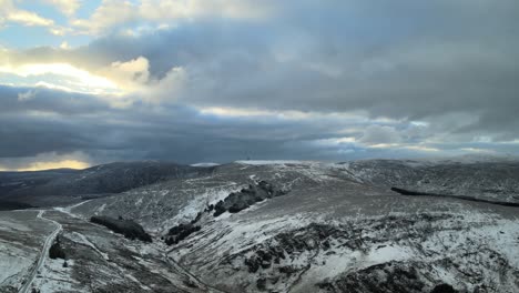 Paisaje-Montañoso-Nevado-Con-Nubes-Y-Luz-Solar-Asomando,-Vista-Aérea