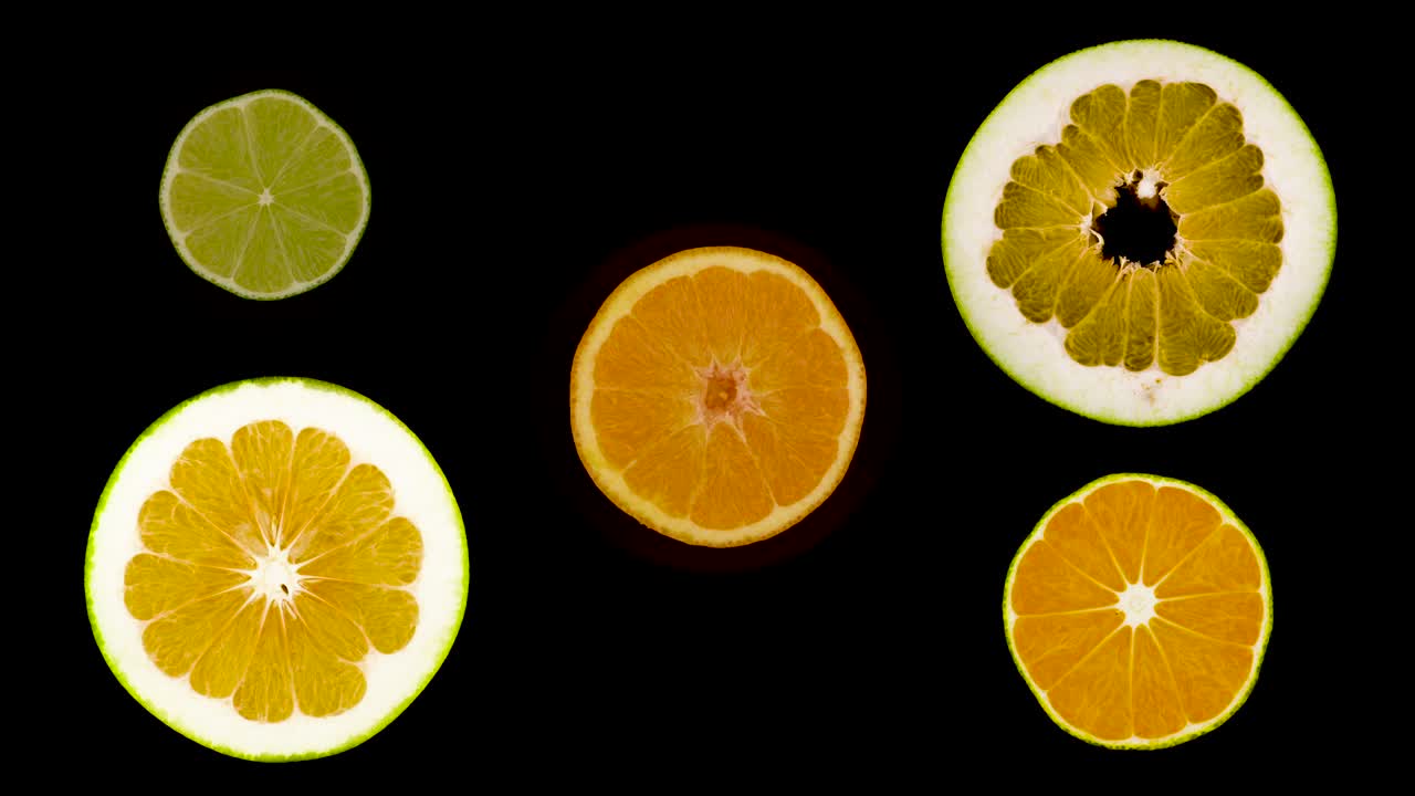 Primo piano di fette di agrumi. Sfondo alimentare estivo. Limone, lime, pompelmo, pomelo, arance. Isolato, su sfondo nero, vista dall'alto. Rotazione