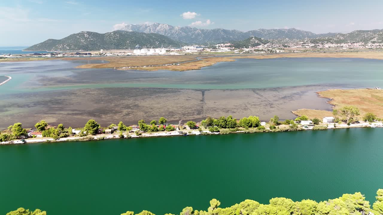 Drone flies backward over the colorful Neretva Delta, revealing the winding river channel bordered by trees and golden sandy shallows in warm sunlight. Croatia