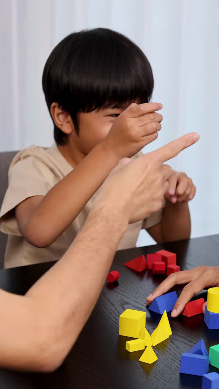 Padre e figlio asiatici giocano con blocchi giocattolo geometrici colorati a casa, con luce naturale.