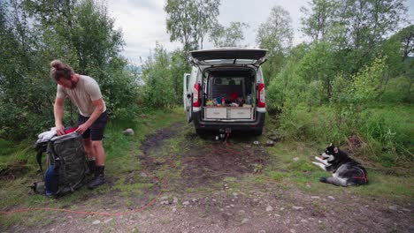 hombre empacando cosas con una autocaravana estacionada en el desierto y un perro malamute de alaska tirado en el suelo