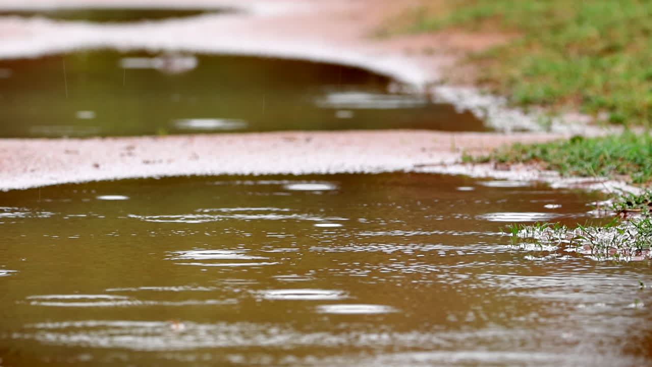 Raindrops splashing into a dirt road puddle on a cloudy day, creating ripples outdoors