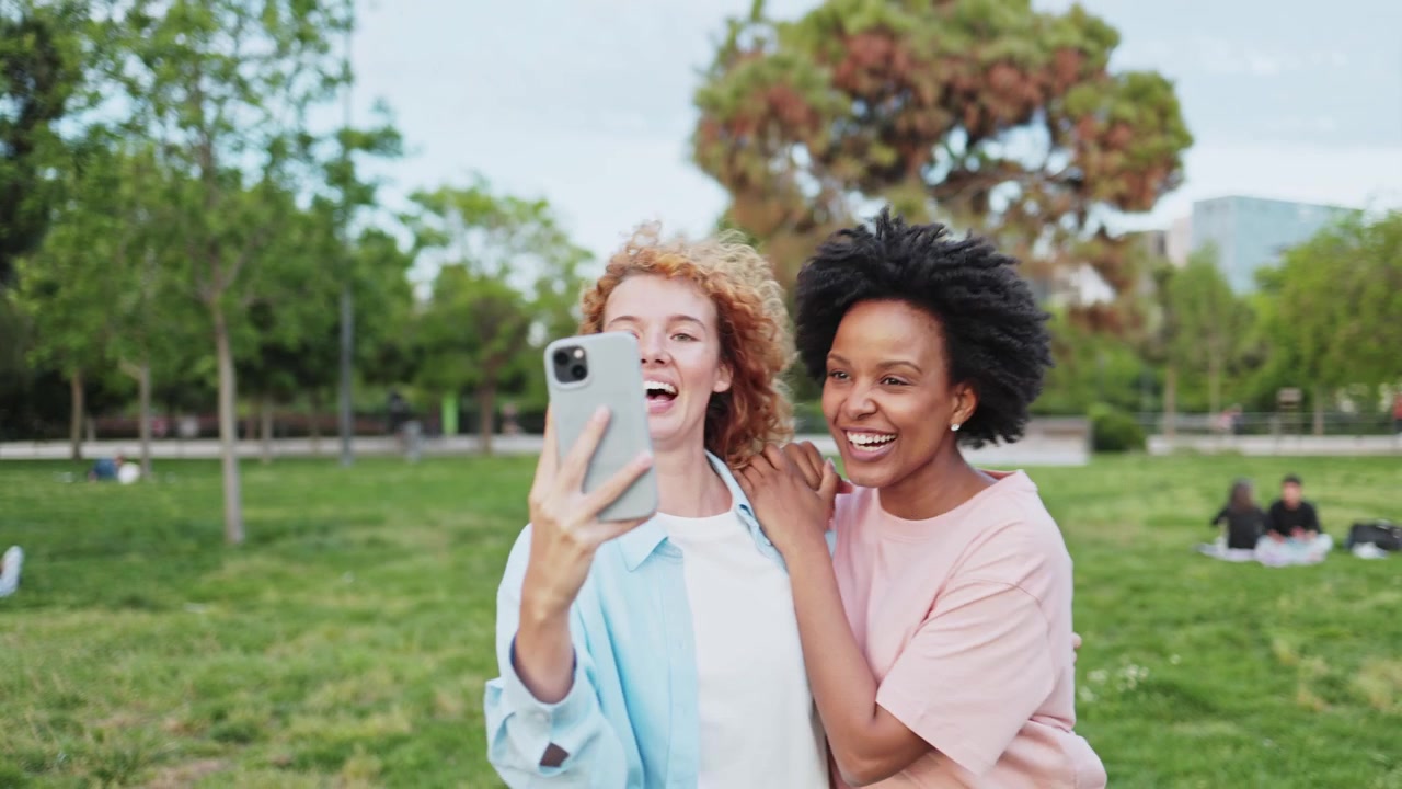 Due donne felici e diverse si scattano un selfie e ridono in un parco.