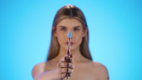 static medium shot of a young beautiful woman or model holding a toothbrush for good and important dental care and dental health into the camera in front of blue background in slow motion