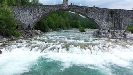 drone flying under gobbo bridge along trebbia river, bobbio in italy