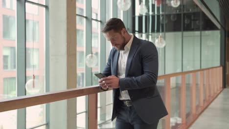 an attractive young, bearded businessman in a blue blazer consults his smart phone attentively and writes on it