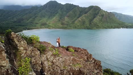 drone shot circling a romantic couple kissing on top of the cliffs on the crouching lion hike on oahu, hawaii