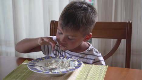 Niño-Bronceado-Caucásico,-Sentado-En-La-Mesa-De-La-Casa-Comiendo-Arroz-Y-Jugando-Con-él-4k