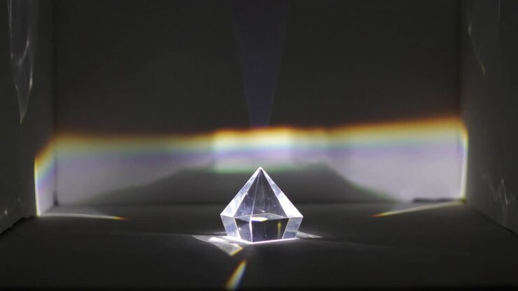 Projecting focused white light hitting clear faceted prism inside white box, casting rainbow band