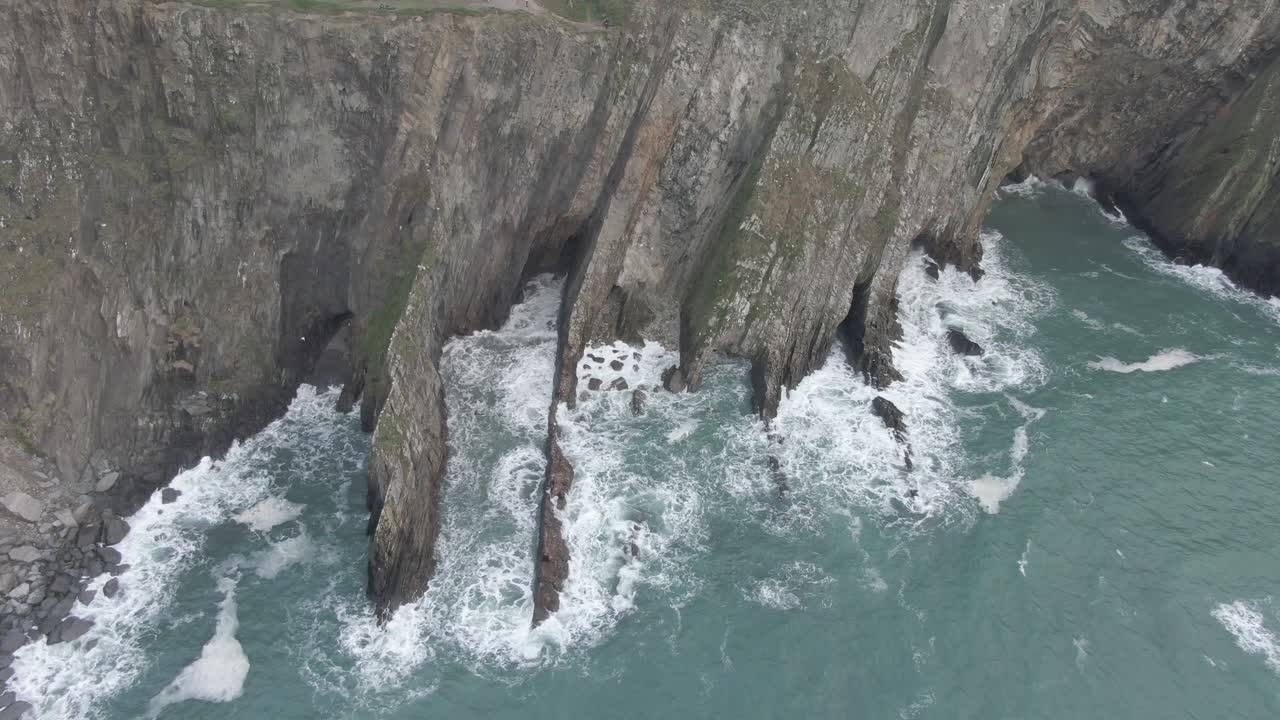 Stationary slow motion aerial view of irish sea side cliffs with rough seas and waves hitting the cliffs