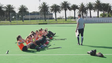 Coach-watching-female-hockey-players-exercising-on-the-field