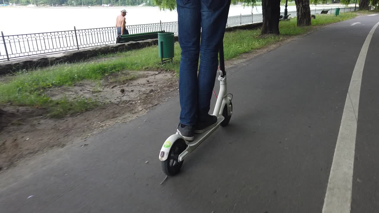 CHISINAU, MOLDAVIA - 9 DE JULIO DE 2019: Hombre montado en un patinete eléctrico blanco en el parque Valea Morilor. Lago al fondo