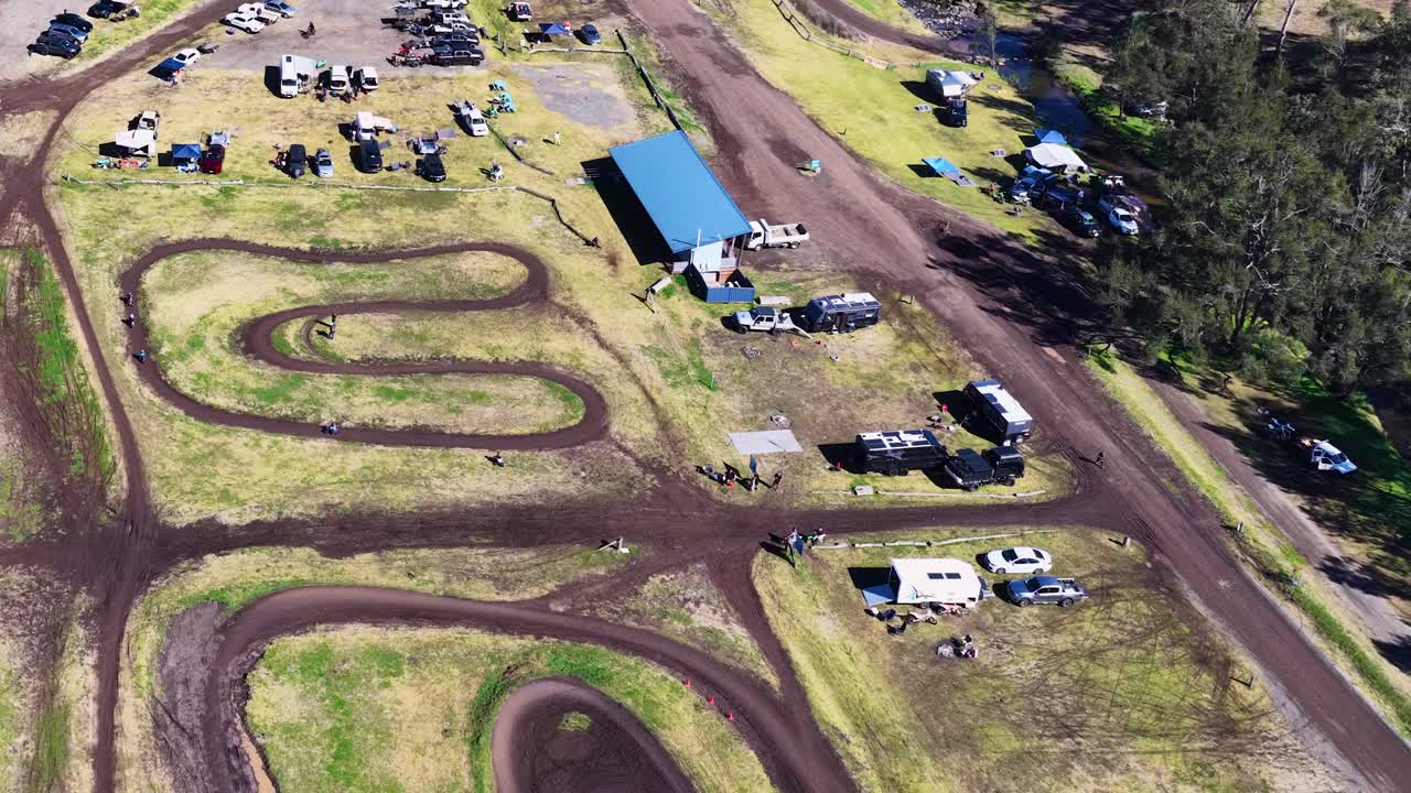 Drone captures motocross track, vehicles, and paddock under bright daylight with smooth aerial movement