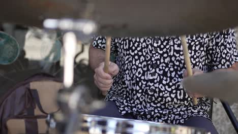 close up of a drummer playing on a drum set, wearing a patterned shirt, with focus on hands and drumsticks