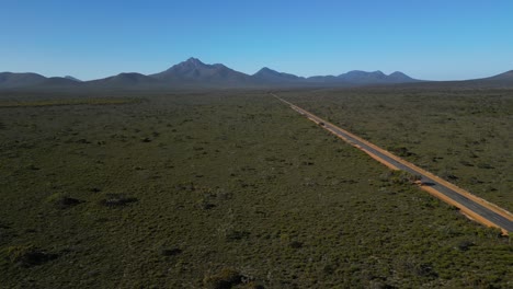 Seguimiento-De-La-Toma-Aérea-De-Una-Carretera-Vacía-En-El-Interior-De-Australia,-Cadenas-Montañosas-En-La-Distancia