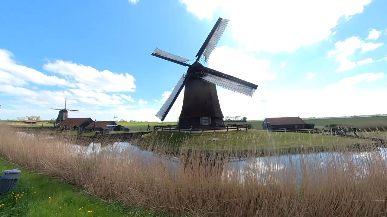 Kincir di Schermerhorn, berputar tertiup angin, kincir kedua di latar belakang. Dua kincir berputar dengan air di depannya. Belanda, kincir air, pompa air. "omdermolen" polder de Schermer dekat Alkmaar
