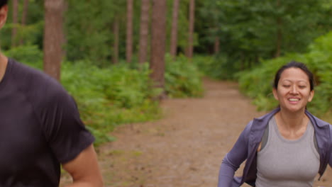 mid adult couple exercising doing work out outdoors running through forest with man encouraging tired woman wearing sports clothing