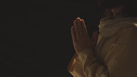 close up of man wearing robes with long hair and beard representing figure of jesus christ putting hands together in prayer