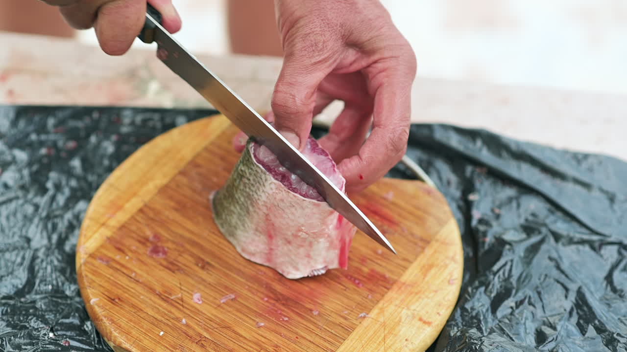 Close up of a man slicing a fish fillet on a wooden cutting board