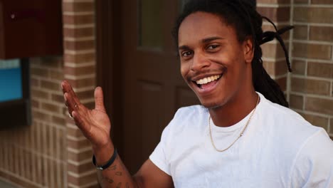 african american man with dreadlocks sitting on bench giving peace sign and smiling and interacting positively with camera