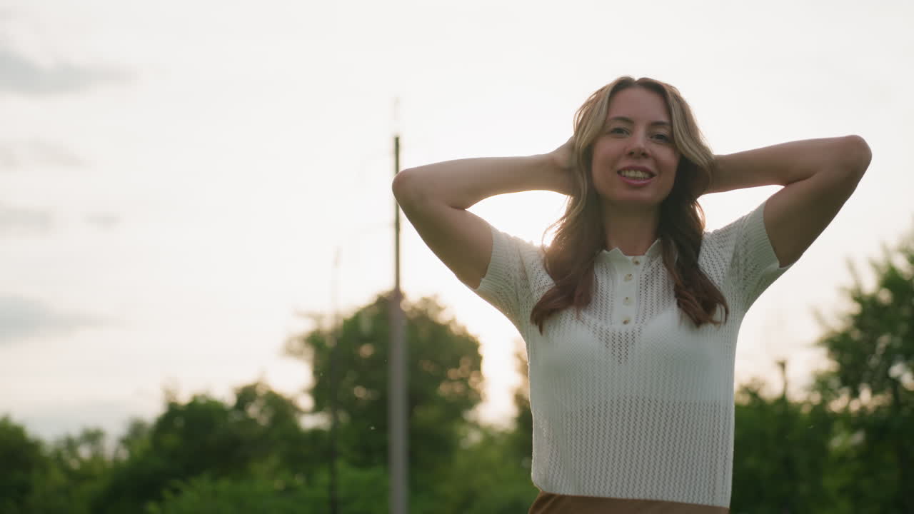 portrait caretaker woman on picnic outing smiling with hands behind head, sun light creating soft glow around hair and face, green trees blurred background, relaxed joyful mood, warm outdoor scene