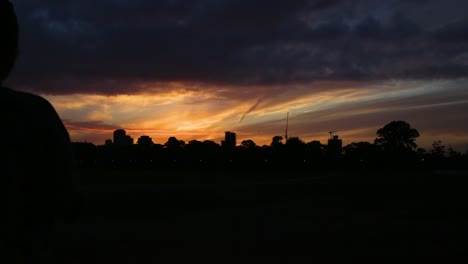 Eine-Junge-Frau-Fotografiert-Mit-Ihrem-Handy-Einen-Sonnenuntergang,-Der-Sich-Gegen-Eine-Lebendige-Stadtlandschaft-Abhebt