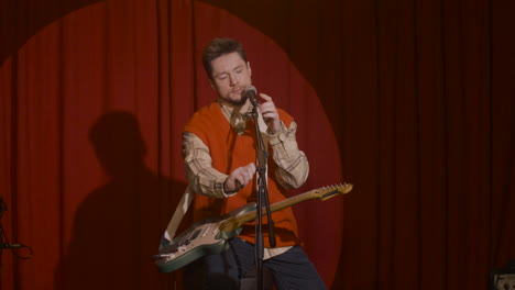 concentrated male musician with guitar and microphone sitting on stool and getting ready for a live performance 2