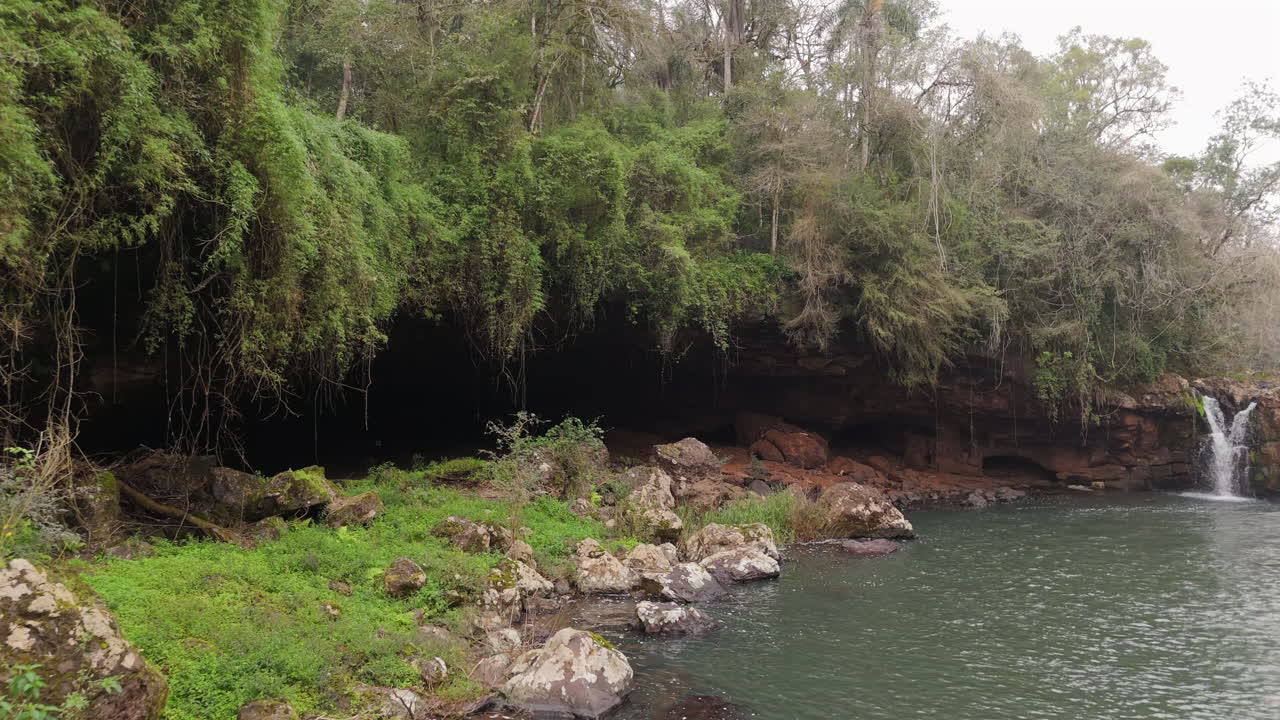 Small waterfall flowing into serene pool surrounded by lush vegetation at Parque Natural Gruta India, Misiones, Argentina.