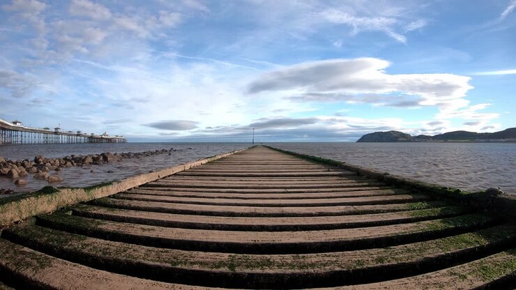 Time lapse waves pulse under empty wooden jetty boardwalk leading to overcast seascape rising shot