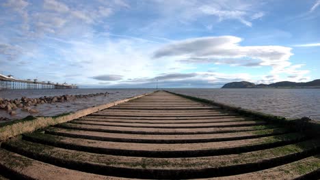 Time-lapse-waves-pulse-under-empty-wooden-jetty-boardwalk-leading-to-overcast-seascape-rising-shot