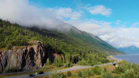 4k drone video of cars travelling on seward highway at base of mountain along shoreline of turnagain inlet near anchorage during summer