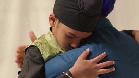 close up studio shot of sikh father embracing son both wearing turbans against plain background