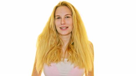 mujer joven con cabello largo y rubio de pie en un estudio blanco, frente a la cámara, sonriendo y posando