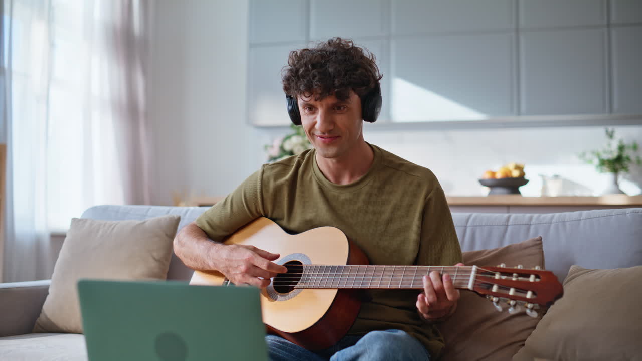 Musisi bahagia bermain gitar di ruang tamu rumah. Pria tersenyum merekam musik