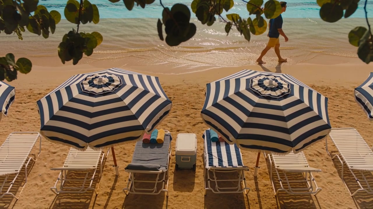 Uomo che entra da sinistra, con camicia blu navy e pantaloncini gialli, che cammina lungo la spiaggia per rilassarsi.