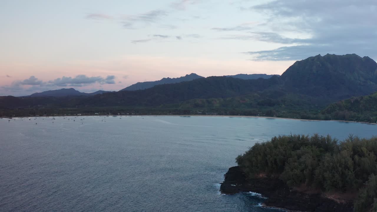 Wide descending aerial shot of peaceful Hanalei Bay from the Pacific Ocean during low light on the island of Kaua'i, Hawai'i